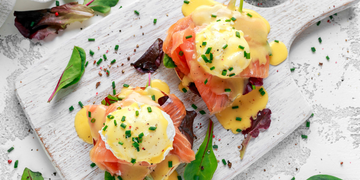 Eggs Benedict on english muffin with smoked salmon, lettuce salad mix and hollandaise sauce on white