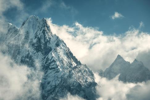 Manaslu mountain with snowy peak in clouds in sunny bright day in Nepal. Landscape with high snow covered rocks and blue cloudy sky. Beautiful nature. Fairy scenery. Aerial view of Himalayan mountains