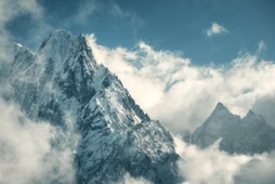 Manaslu mountain with snowy peak in clouds in sunny bright day in Nepal. Landscape with high snow covered rocks and blue cloudy sky. Beautiful nature. Fairy scenery. Aerial view of Himalayan mountains