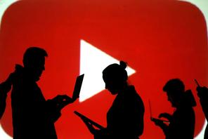 Silhouettes of laptop and mobile device users are seen next to a screen projection of Youtube logo i