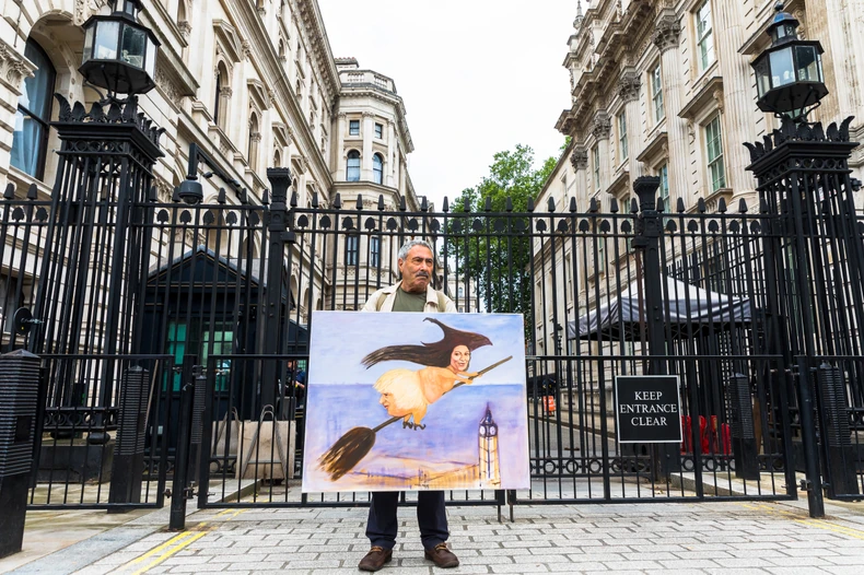 Britanci frustrirani zbog pandemijskih pravila: satiričar Kaja Mar ispred Dauning strita sa slikom premijera Borisa Džonsona na veštičjoj metli