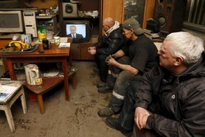 Workers watch a TV broadcast of Russian President Putin address to the Federal Assembly at an auto r