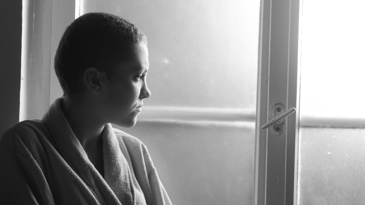 Young depressed cancer patient standing in front of hospital window