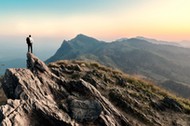 businessman hike on the peak of rocks mountain at sunset