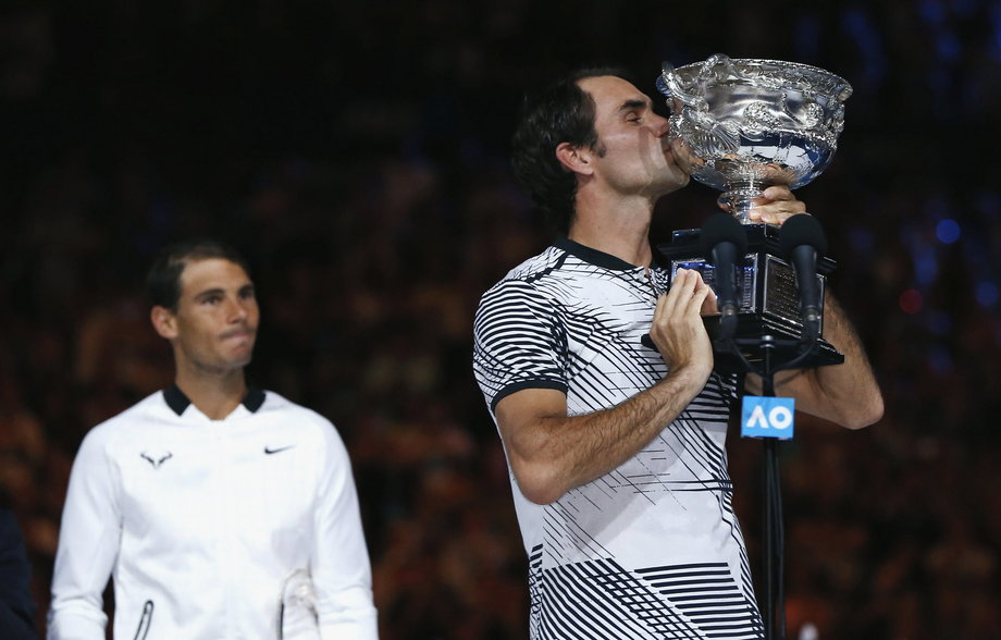 Rafael Nadal watches as Roger Federer kisses the Australian Open trophy.