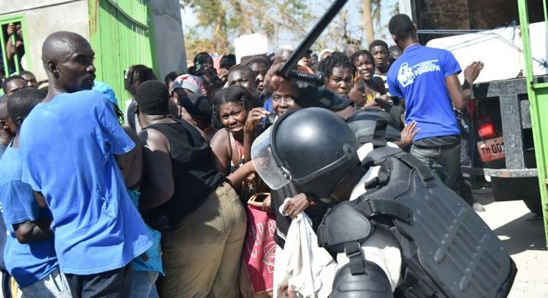 A Haitian policeman pushes back Hurricane Matthew victims waiting for the delivery of food from the UN's World Food Programme in Tobeck, in Les Cayes