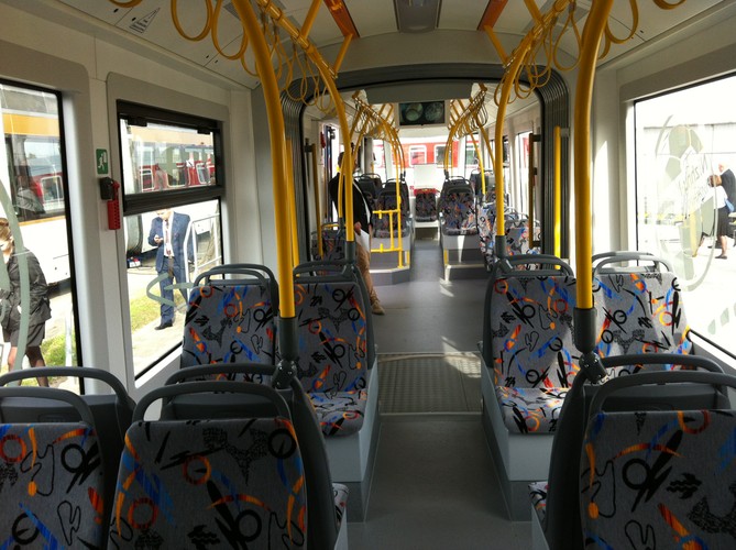 Pstrokate fotele i żółte poręcze. Tak wygląda Fokstrot w środku. Każdy z pojazdów ma niespełna 27 metrów długości. Pomieszczą 190 osób, w tym 60 na miejscach siedzących. Na życzenie władz Moskwy na szybach naklejone są wielkie, propagandowe piłki z nazwami miast-gospodarzy mundialu w Rosji w 2016 r., który może zostać przeniesiony do innego kraju w ramach sankcji po agresji na Ukrainie. Fot. Konrad Majszyk