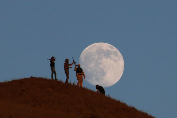 Free Syrian army fighters stand atop of a hill as the moon is seen in the background in the south of