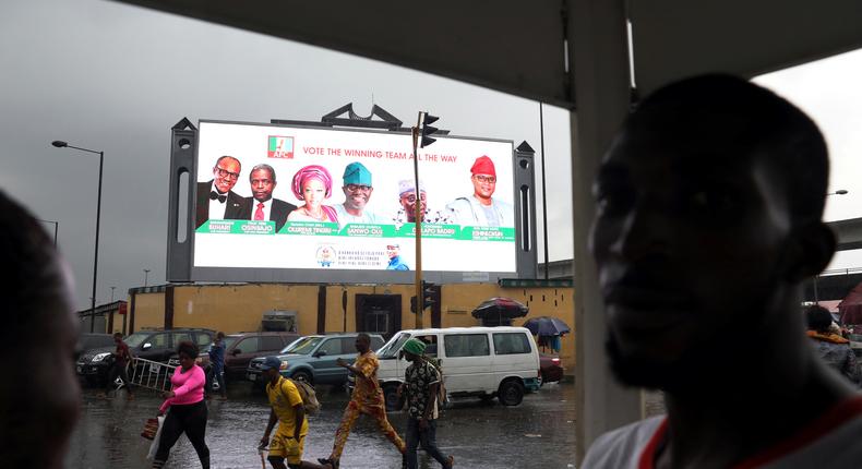 People walk past a campaign billboard as Nigerians await the result of the Presidential election in Lagos [REUTERS/Temilade Adelaja]