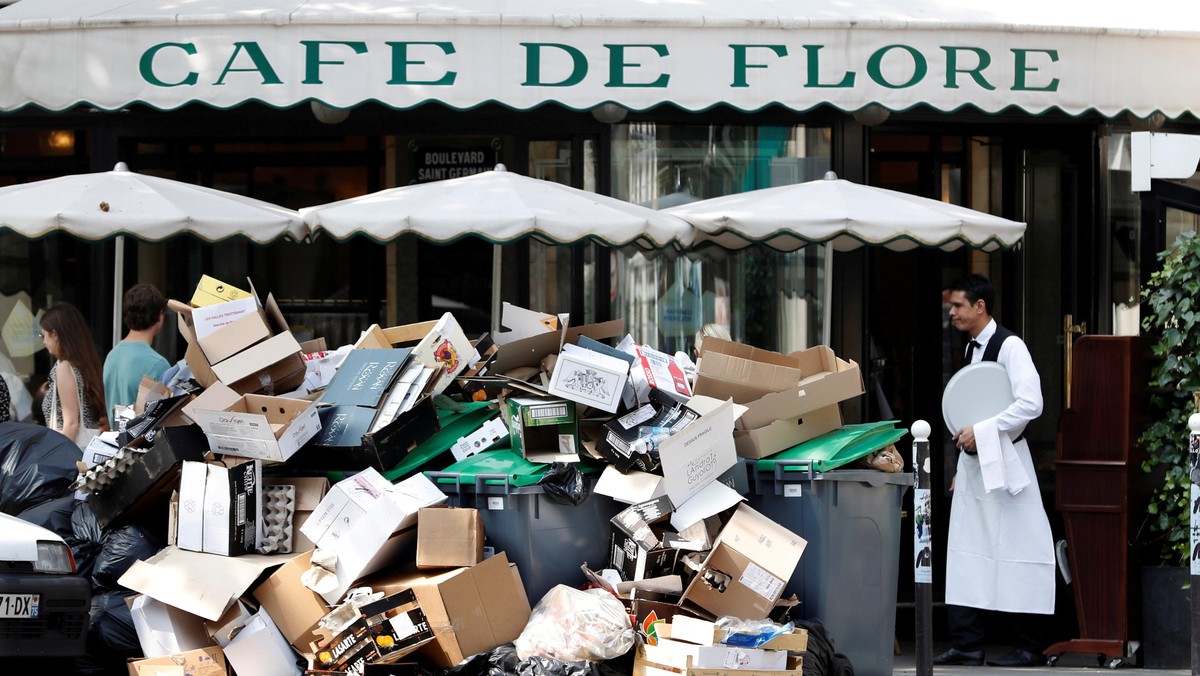 A waiter stands near a pile of rubbish bags in front of the Cafe de Flore in Paris during a strike of garbage collectors and sewer workers of the city of Paris to protest the labour reforms law proposal