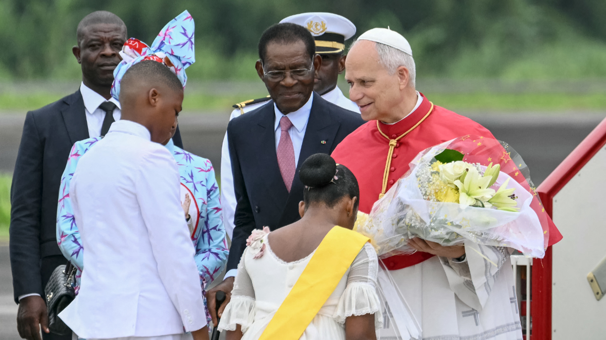 Pope Leo XIV (R) receives flowers from children as he is welcomed by Equatorial Guinea's President Teodoro Obiang Nguema Mbasogo (C) upon his arrival at the Malabo International Airport in Malabo on the ninth day of an 11-day apostolic journey to Africa, on April 21, 2026. [Photo by Alberto PIZZOLI / AFP via Getty Images]