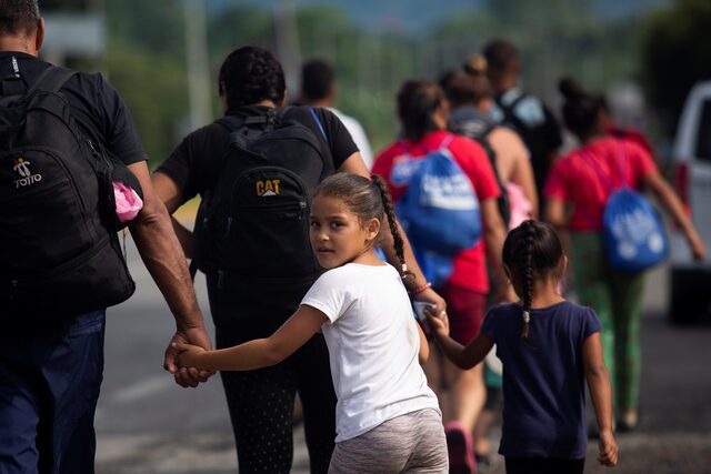 Children hold their parents' hands as they walk with other migrants in a caravan toward the U.S. border. [ Image Credit: REUTERS/Quetzalli Nicte-Ha]