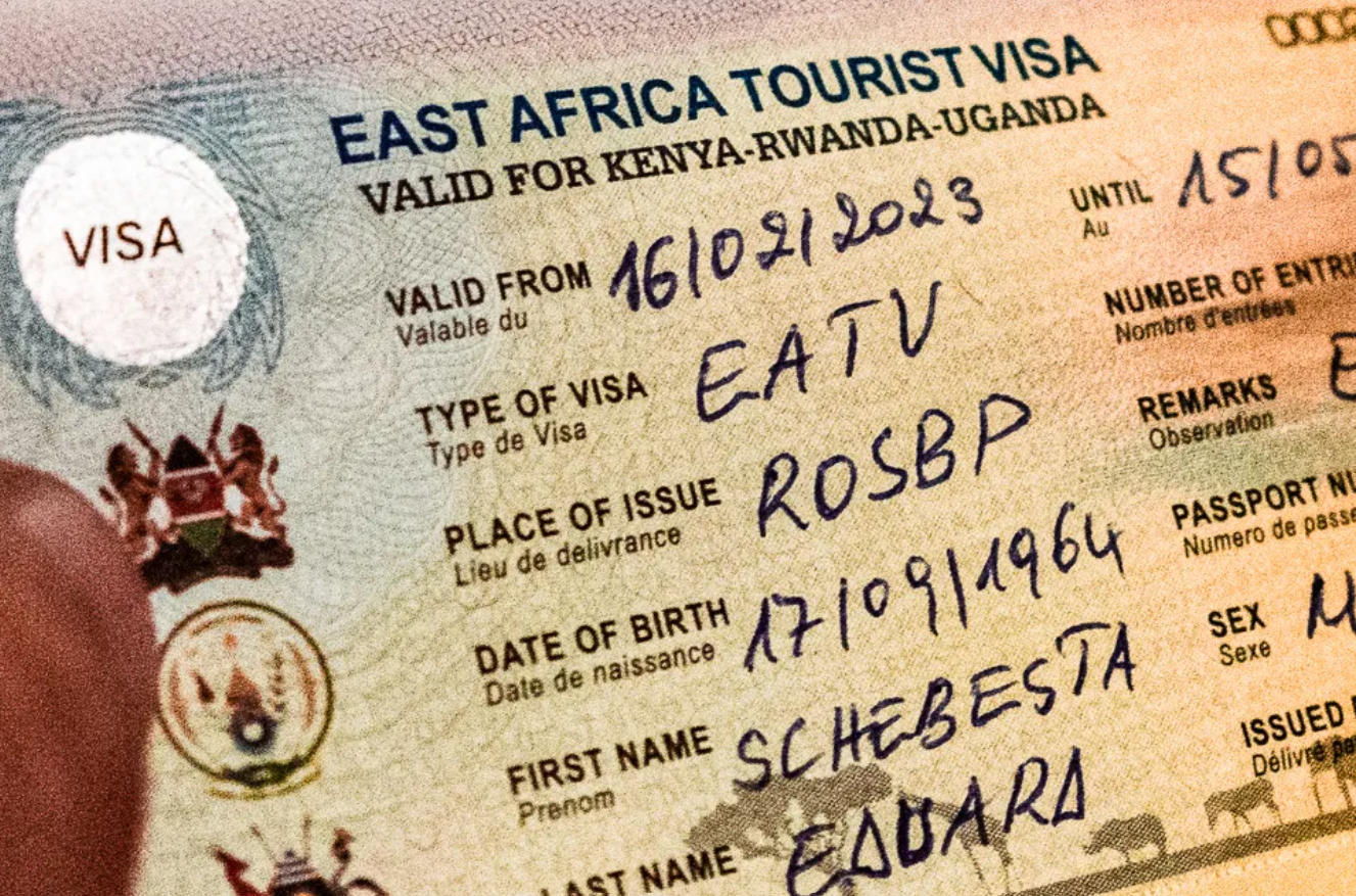 A filled-out specimen of an East Africa Tourist Visa (EATV) sticker affixed to a passport page, detailing regional entry privileges for Kenya, Rwanda, and Uganda. Image courtesy of Ngavu Tours.