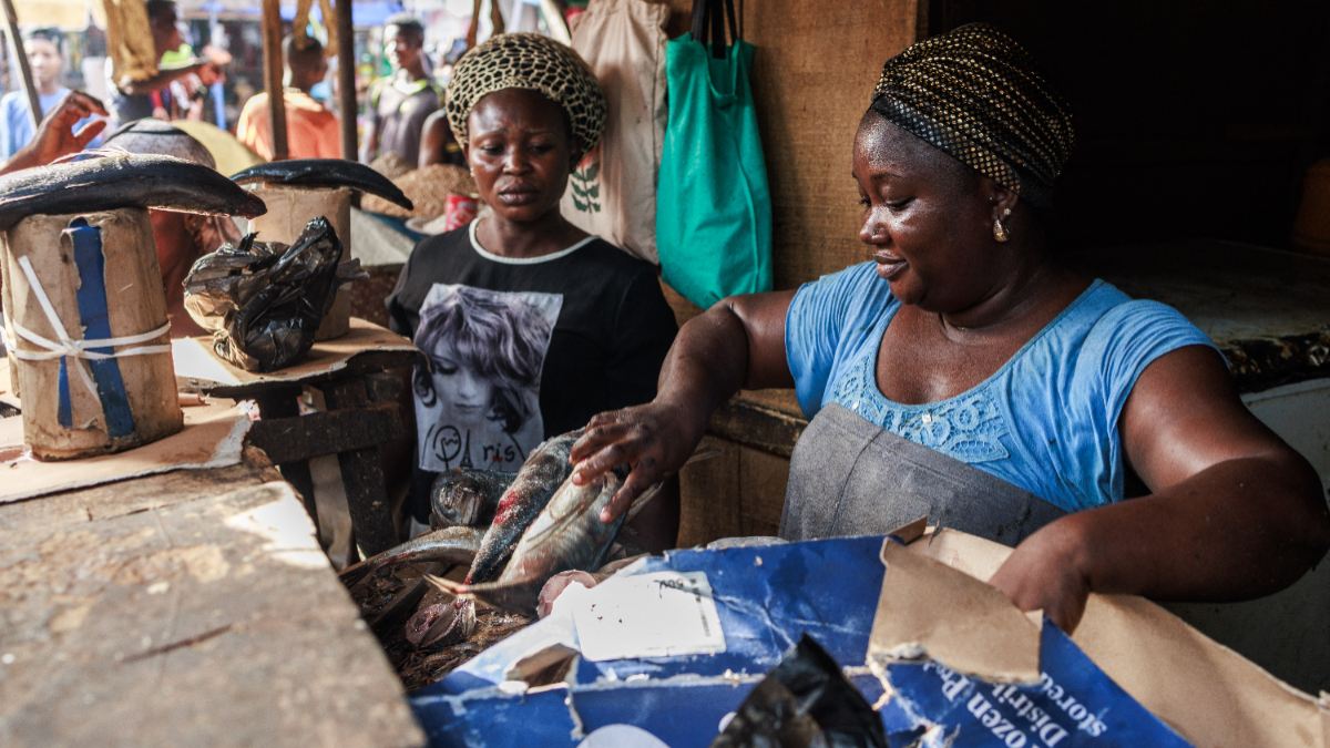 A woman selling fresh fish prepares some pieces for a client at a market in the Obalende area of Lagos on December 18, 2023. [Photo by BENSON IBEABUCHI/AFP via Getty Images]