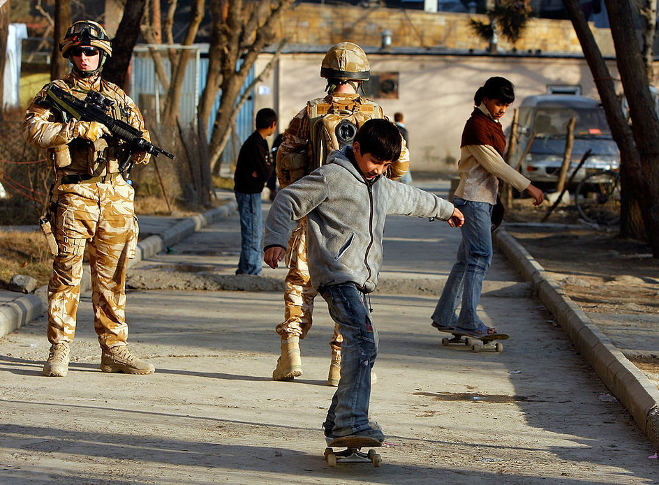 Chłopiec na deskorolce w Kabulu. W tle żołnierze