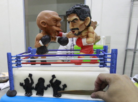 A cake decorator places details on a two-layer cake featuring fondant caricatures of boxers Manny Pacquiao (R) of the Philippines and Floyd Mayweather of the U.S. inside a boxing ring in Manila