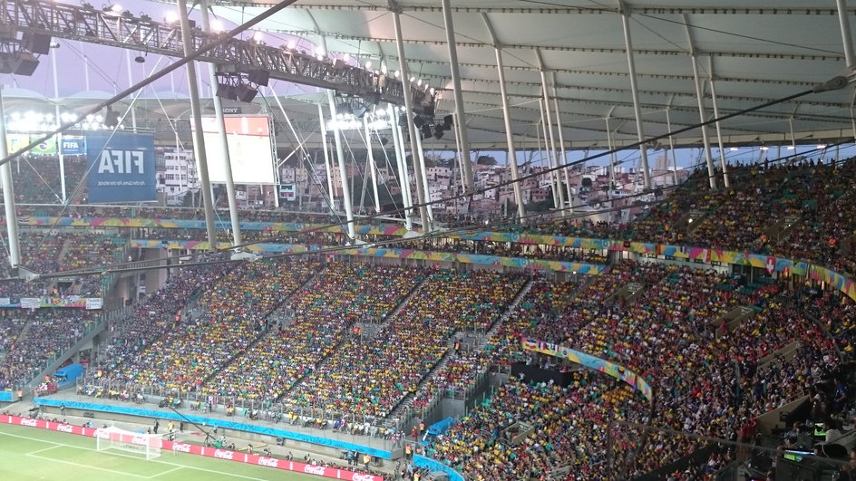 Jedna z trybun stadionu w Salvadorze z prześwitującymi fawelami w tle