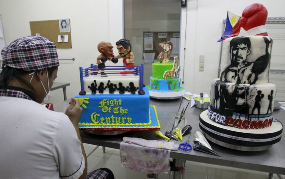 Cake decorator places details on a two-layer cake featuring fondant caricatures of boxers Pacquiao of the Philippines and Mayweather of the U.S. inside a boxing ring at a bakery in Manila