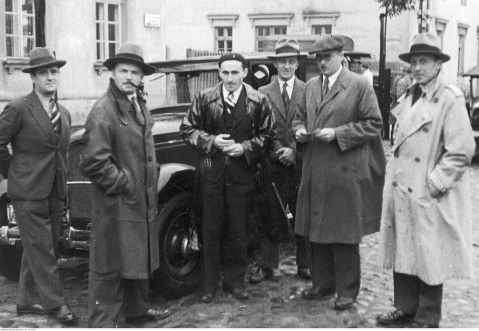 Janusz Kusociński (w skórzanym płaszczu) po zdaniu egzaminu na prawo jazdy w 1932 roku stoi przy swoim samochodzie marki Buick w towarzystwie członków komisji egzaminacyjnej.