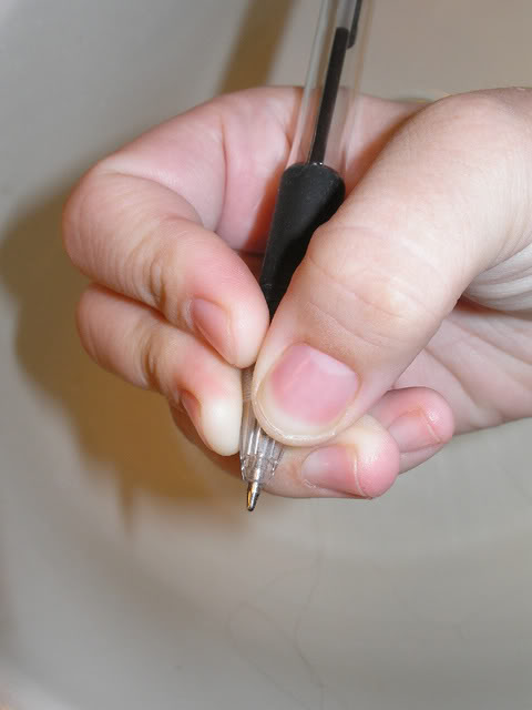 trzymając długopis przez koniuszki palca wskazującego i środkowego z jednej strony oraz kciuka z drugiej strony